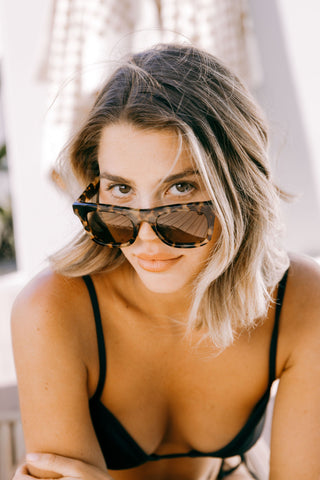 Woman in black bikini wears brown tortoiseshell biodegradable and sustainable sunglasses with tan lens