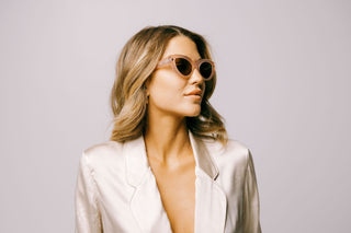 Woman in cream silk top wears pink Cleo Floss cateye biodegradable and sustainable sunglasses with tan lens