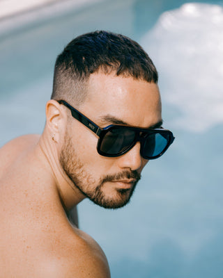 man by a swimming pool wears large black sustainable and biodegradable malone charcoal aviator sunglasses with dark grey lens